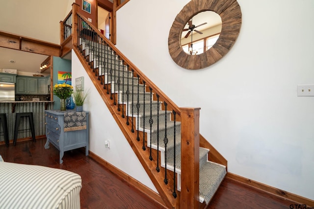 stairs with a high ceiling, a ceiling fan, baseboards, and wood finished floors
