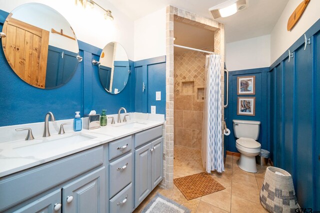 full bathroom with double vanity, a tile shower, toilet, and a sink