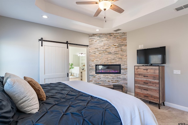 bedroom with carpet floors, a tray ceiling, a barn door, and visible vents