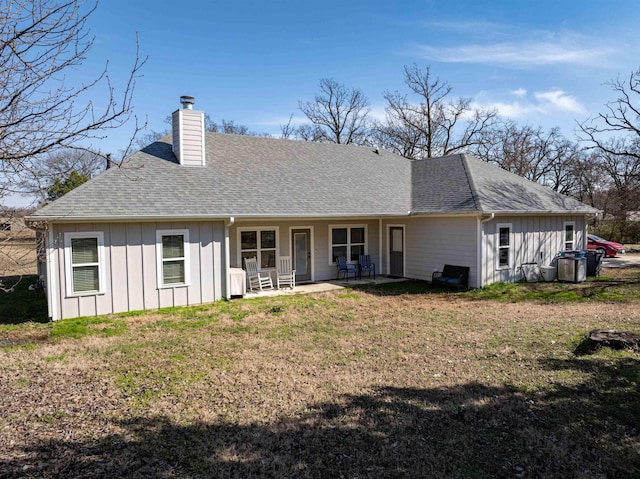 back of property with a patio, roof with shingles, a lawn, board and batten siding, and a chimney