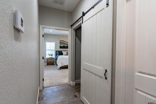 hall with hardwood / wood-style floors, a textured wall, a barn door, and visible vents