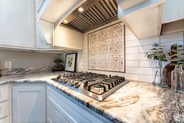 kitchen featuring white cabinets, custom range hood, stainless steel gas cooktop, and decorative backsplash