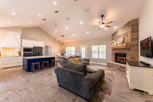 living room featuring ceiling fan, high vaulted ceiling, a stone fireplace, visible vents, and light wood-type flooring