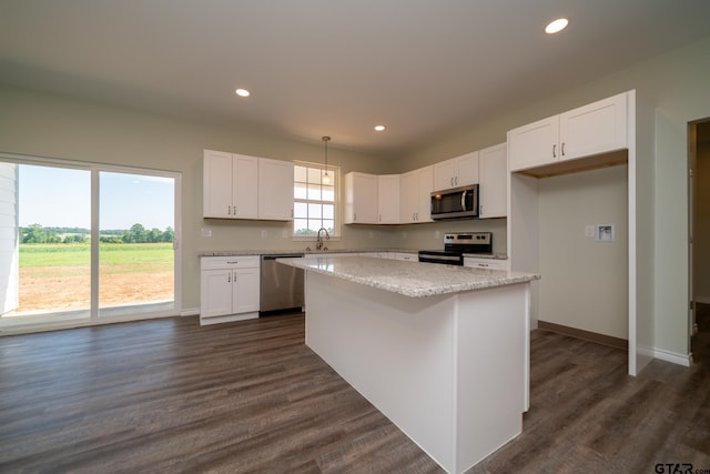 kitchen with light stone counters, stainless steel appliances, a kitchen island, white cabinetry, and dark hardwood / wood-style flooring