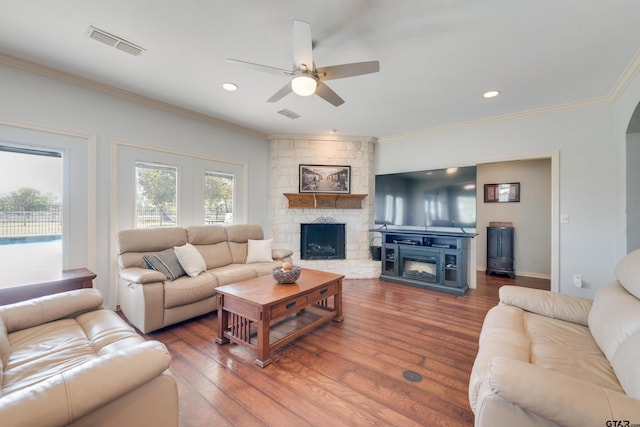 living room with a stone fireplace, ornamental molding, hardwood / wood-style floors, and ceiling fan