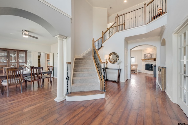 foyer entrance with a large fireplace, dark hardwood / wood-style flooring, ceiling fan, and crown molding