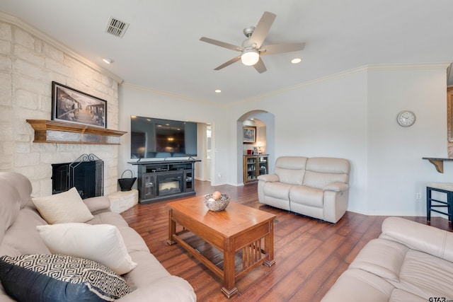 living room featuring dark wood-type flooring, a stone fireplace, ceiling fan, and ornamental molding