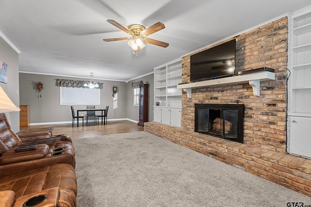 living area with crown molding, a brick fireplace, wood finished floors, baseboards, and ceiling fan with notable chandelier