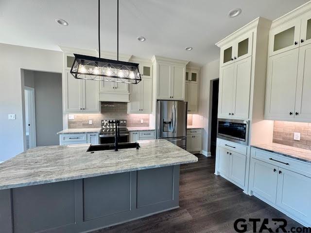 kitchen with light stone countertops, dark wood finished floors, a center island with sink, appliances with stainless steel finishes, and a sink