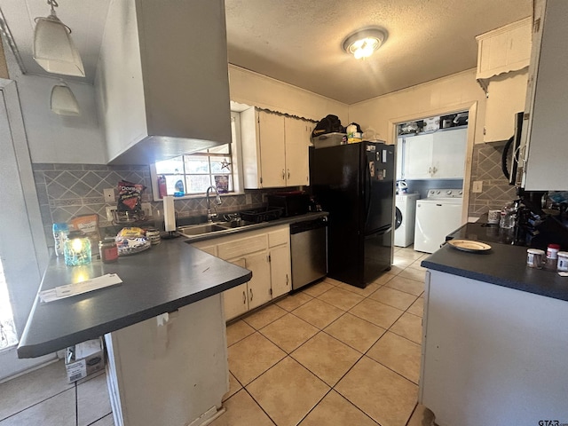 kitchen featuring washing machine and clothes dryer, dark countertops, a peninsula, stainless steel appliances, and a sink