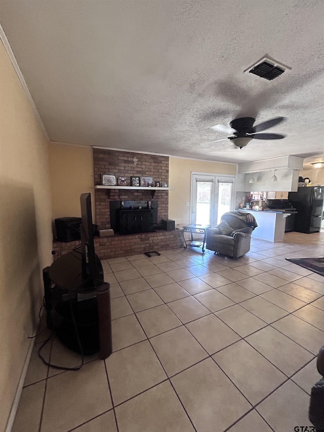 living room featuring visible vents, a ceiling fan, a textured ceiling, a fireplace, and light tile patterned floors