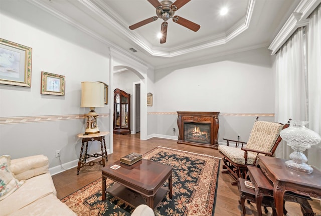 living room with light hardwood / wood-style floors, ceiling fan, a raised ceiling, and crown molding