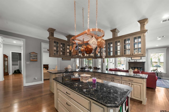 kitchen with kitchen peninsula, ornamental molding, dark hardwood / wood-style floors, a kitchen island, and dark stone countertops