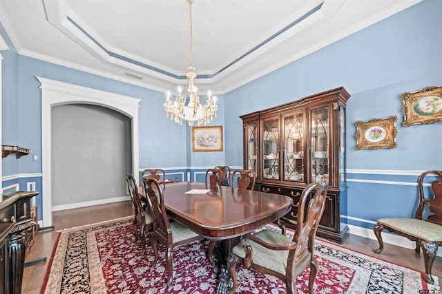 dining room featuring hardwood / wood-style flooring, a raised ceiling, an inviting chandelier, and ornamental molding