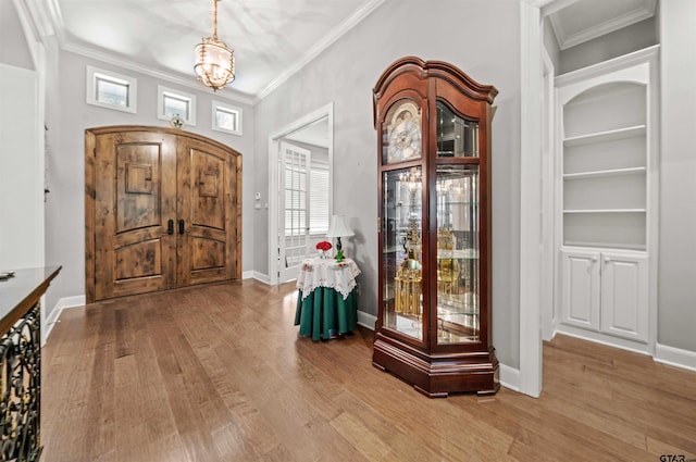 foyer entrance with light hardwood / wood-style flooring, crown molding, and an inviting chandelier