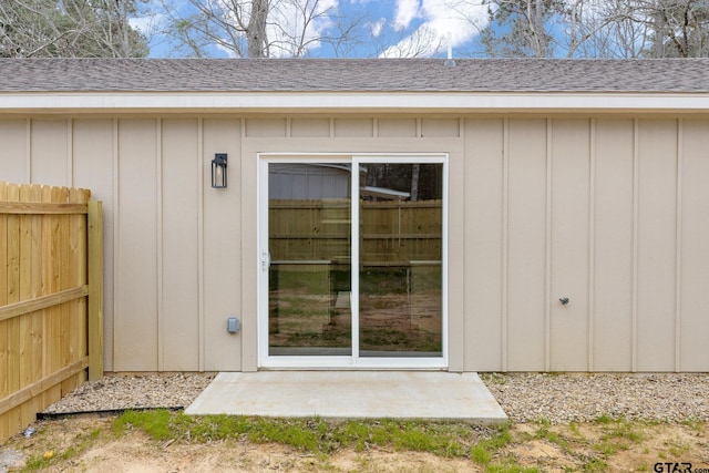 doorway to property with board and batten siding, fence, and a shingled roof