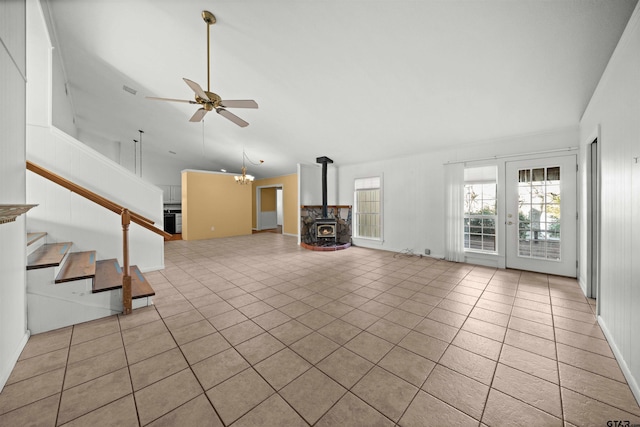 unfurnished living room featuring vaulted ceiling, ceiling fan with notable chandelier, a wood stove, and light tile patterned floors