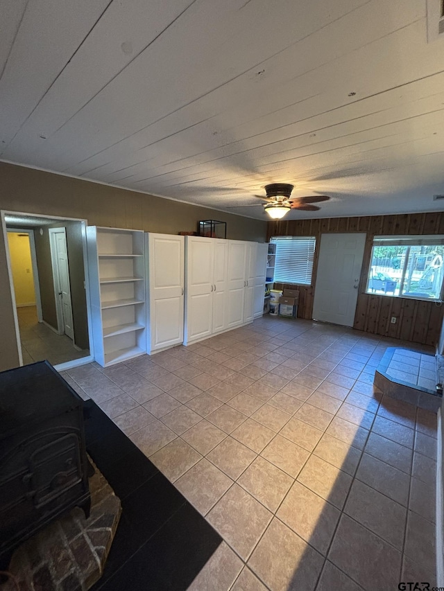 606 Glazner St, Hawkins, TX 75765 - unfurnished living room featuring built in features, a wood stove, light tile patterned flooring, wooden walls, and a ceiling fan