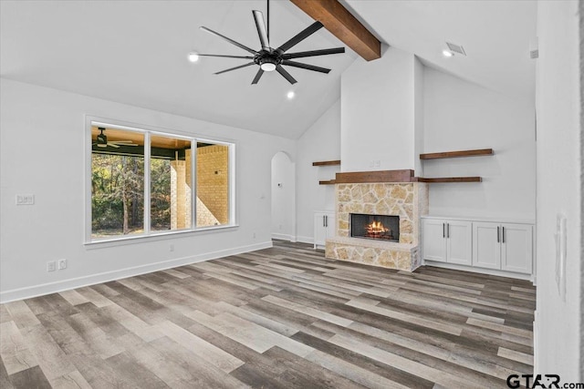 unfurnished living room featuring beamed ceiling, a stone fireplace, light wood-type flooring, and high vaulted ceiling