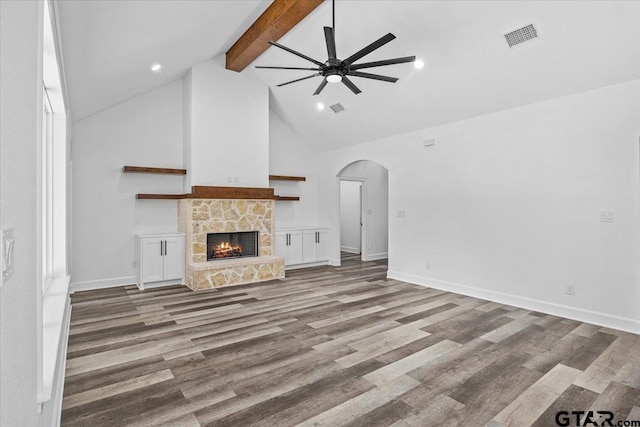 unfurnished living room with a stone fireplace, ceiling fan, hardwood / wood-style floors, and beamed ceiling