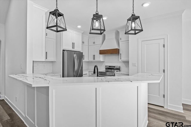 kitchen with kitchen peninsula, appliances with stainless steel finishes, premium range hood, white cabinets, and hanging light fixtures