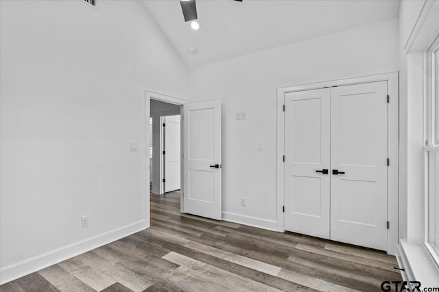 unfurnished bedroom featuring hardwood / wood-style flooring, ceiling fan, high vaulted ceiling, and a closet