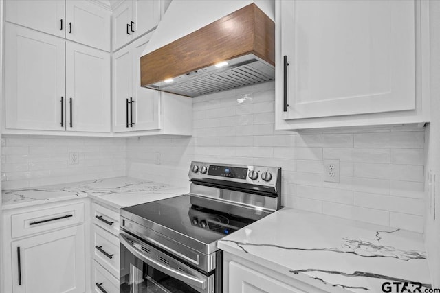 kitchen featuring light stone countertops, premium range hood, stainless steel range with electric stovetop, decorative backsplash, and white cabinets