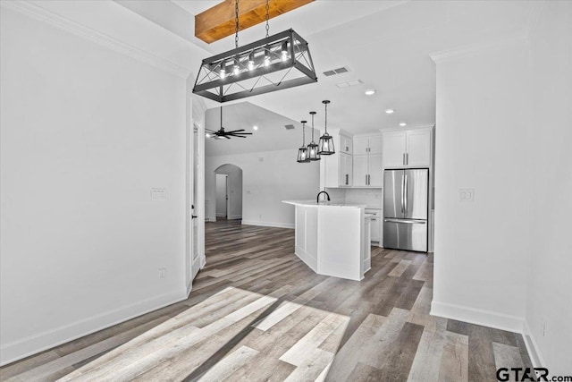 kitchen with a kitchen island with sink, white cabinets, ceiling fan, stainless steel fridge, and decorative light fixtures