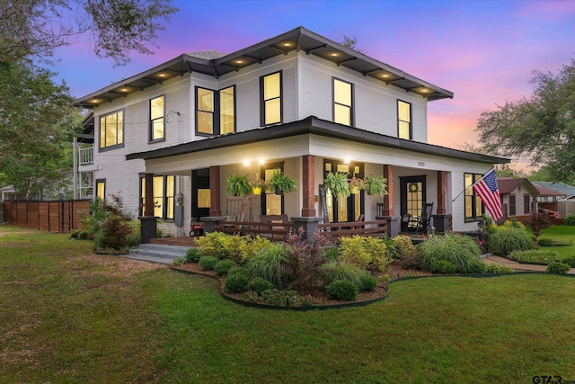 back house at dusk featuring a lawn and covered porch