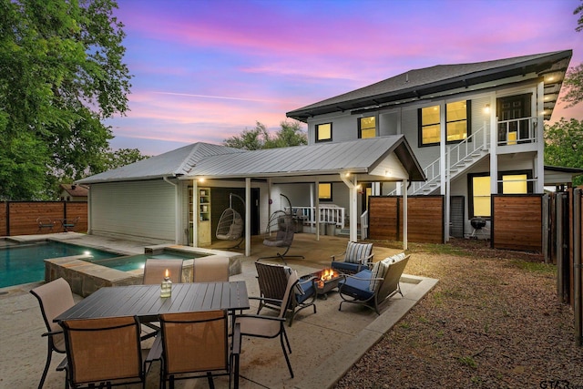 back house at dusk featuring a pool with hot tub and a patio