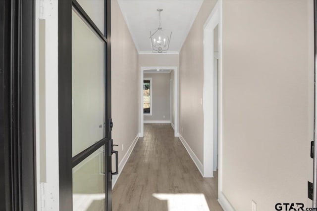 corridor with ornamental molding, an inviting chandelier, and light wood-type flooring