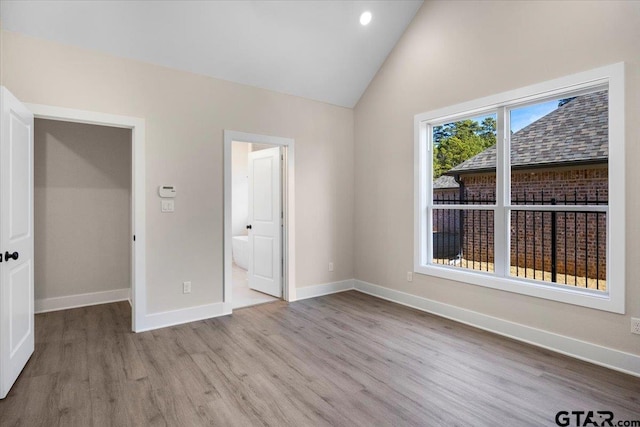 unfurnished bedroom with vaulted ceiling, a spacious closet, ensuite bathroom, and light wood-type flooring