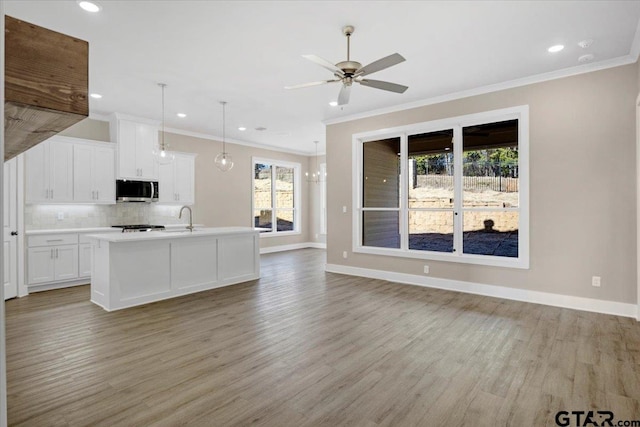 kitchen featuring pendant lighting, tasteful backsplash, white cabinetry, a kitchen island with sink, and light hardwood / wood-style flooring