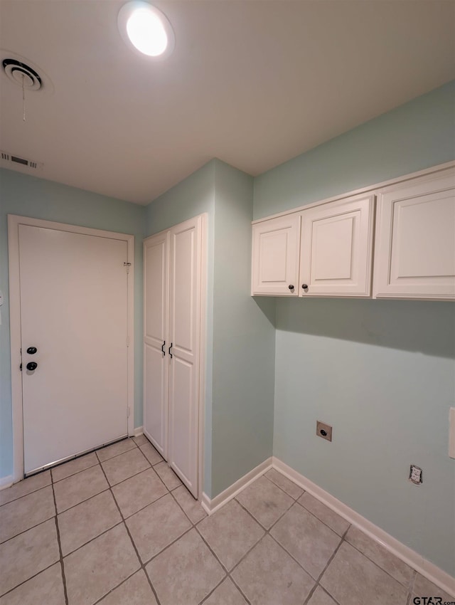 laundry area with electric dryer hookup, light tile patterned floors, and cabinets