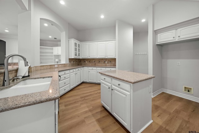 kitchen with decorative backsplash, light stone countertops, sink, white cabinets, and a center island