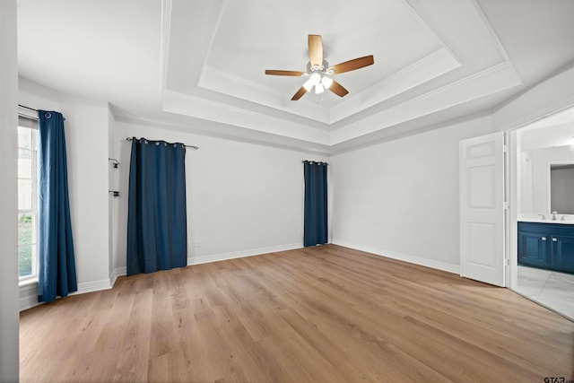 empty room with ceiling fan, light hardwood / wood-style flooring, sink, and a tray ceiling