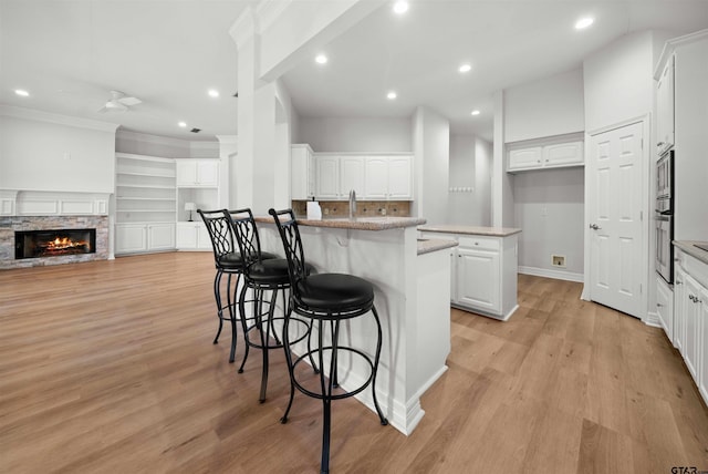 kitchen featuring appliances with stainless steel finishes, white cabinets, a stone fireplace, a breakfast bar area, and an island with sink