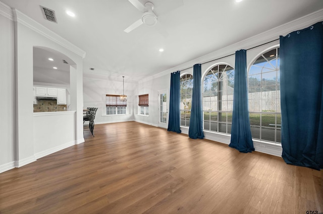 unfurnished living room featuring ceiling fan with notable chandelier, ornamental molding, and dark wood-type flooring