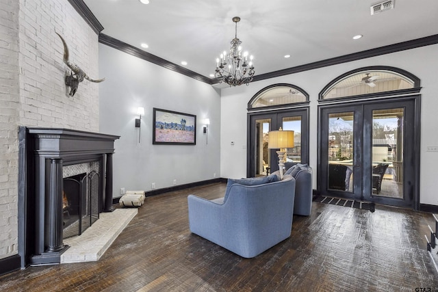 living room with french doors, dark wood-type flooring, crown molding, a brick fireplace, and a notable chandelier