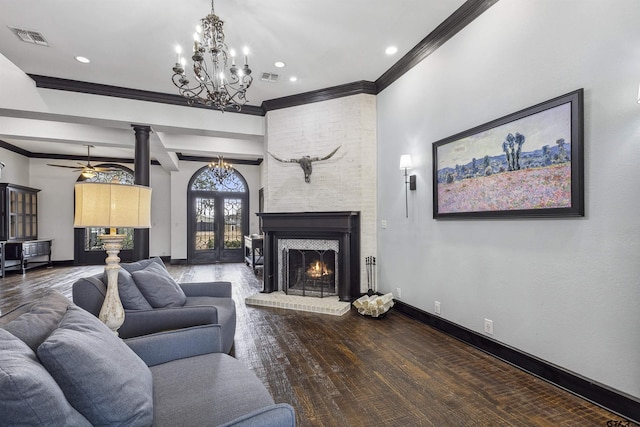 living room featuring wood-type flooring, ornamental molding, beamed ceiling, a fireplace, and ceiling fan with notable chandelier