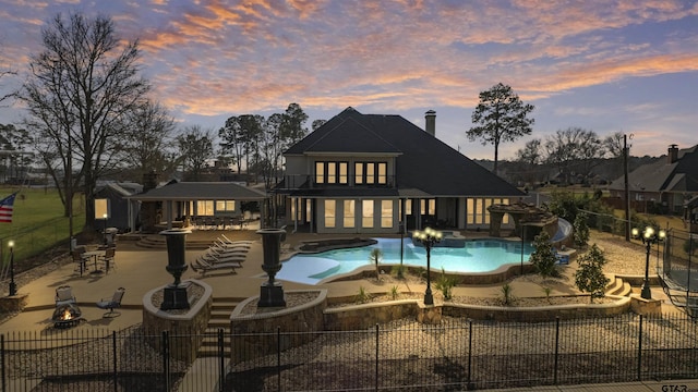 back house at dusk featuring a fenced in pool, a fire pit, a patio area, and a gazebo