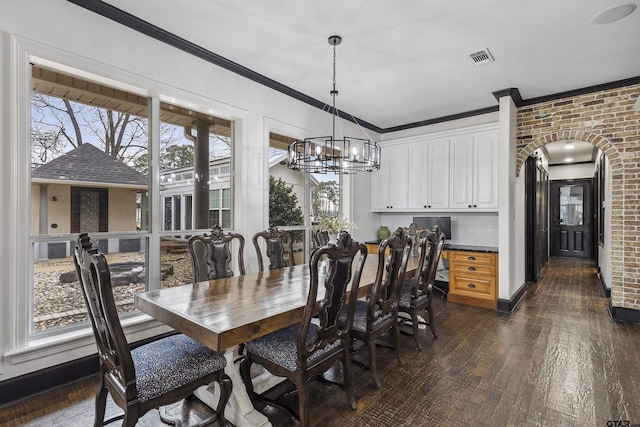 dining space with dark hardwood / wood-style flooring, a notable chandelier, crown molding, and brick wall