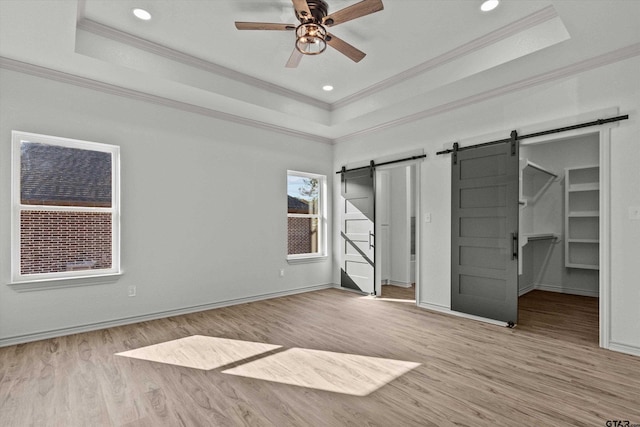 unfurnished bedroom featuring a tray ceiling, a barn door, a spacious closet, and ceiling fan