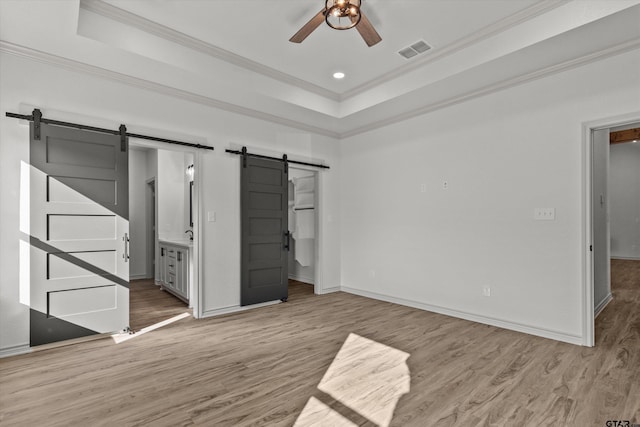 unfurnished bedroom featuring ensuite bathroom, crown molding, ceiling fan, a barn door, and a tray ceiling