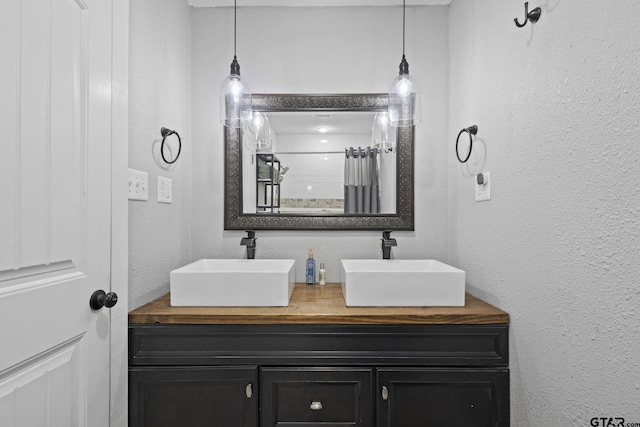 bathroom featuring double vanity, a textured wall, a shower with curtain, and a sink