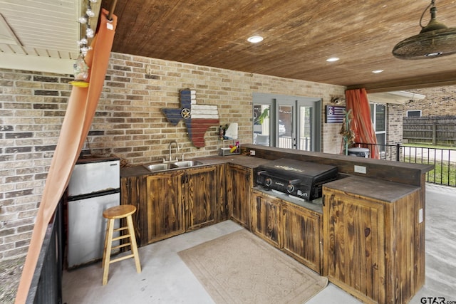 bar featuring freestanding refrigerator, brick wall, wooden ceiling, and a sink