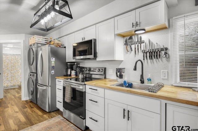 kitchen featuring butcher block counters, stacked washer / dryer, white cabinets, and appliances with stainless steel finishes