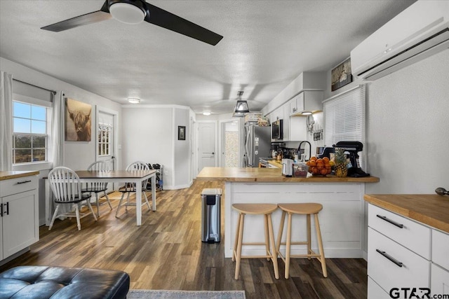 kitchen with white cabinetry, appliances with stainless steel finishes, butcher block countertops, and a wall unit AC