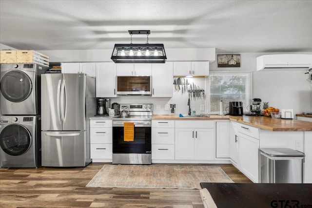 kitchen featuring stacked washer and clothes dryer, butcher block counters, an AC wall unit, appliances with stainless steel finishes, and pendant lighting