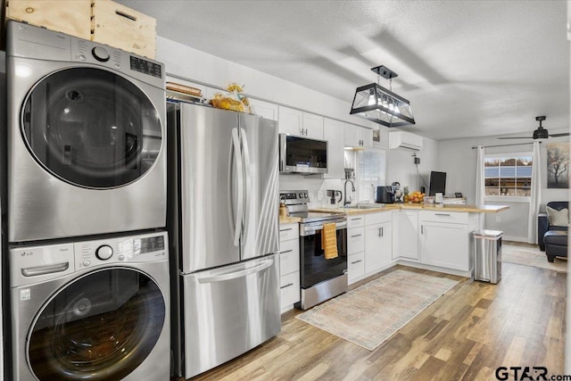 kitchen with decorative light fixtures, stacked washer / dryer, white cabinetry, kitchen peninsula, and stainless steel appliances